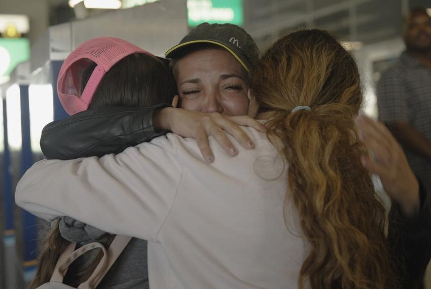 A crying mother hugs her two teenaged daughters.
